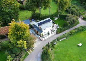 Aerial image of a modern new build cottage exterior with surrounding greenery and road.