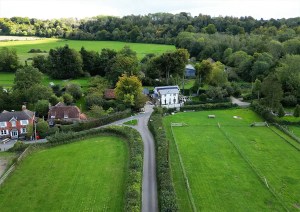 Aerial shot of a modern white cottage positioned within open green fields and countryside.