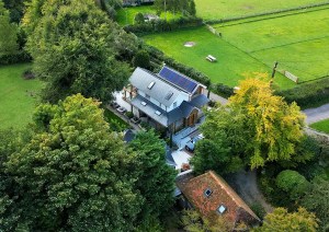 Aerial angle of a modern cottage new build surrounded by mature trees and gardens.
